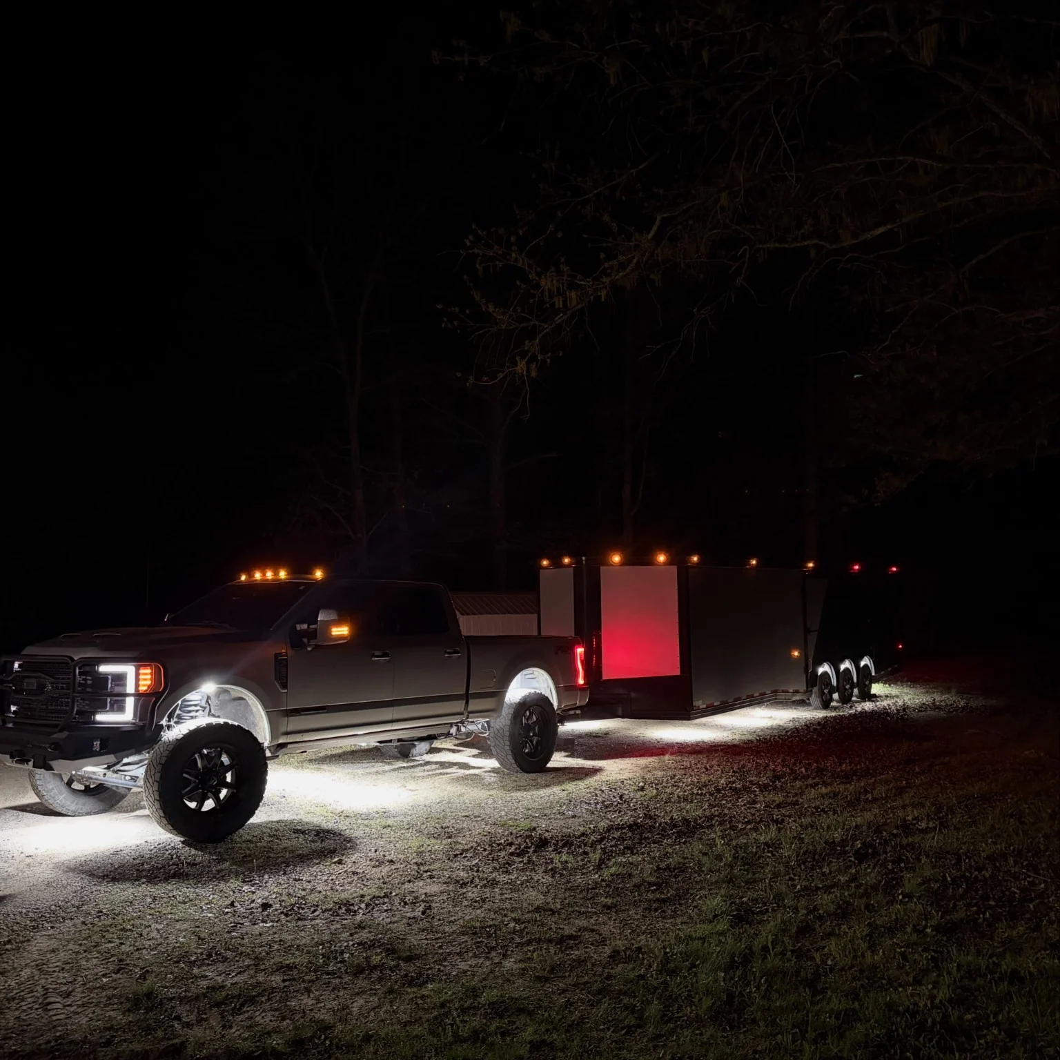 Lifted Ford truck with enclosed trailer and illuminated ground at night
